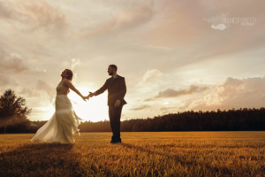 Two people holding hands in a field with a beautiful sunset